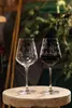 Two wine glasses on a wooden surface, with greenery in the background. Produktbild-Vorschau