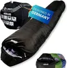 A black mummy sleeping bag is shown diagonally across a white background, with its storage bag and a tag indicating "DESIGNED IN GERMANY" in the upper left. Smaller sleeping bags in different colors are visible in the bottom right corner. Produktbild-Vorschau