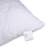 A close-up of a white quilted pillow with a care label attached. Náhled obrázku produktu