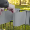 Hands installing grey privacy screen strips onto a wire fence in a garden. Produktbild-Vorschau