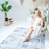 A woman is sitting in a hanging chair in a bright, airy room with a rug on the floor. Náhled obrázku produktu