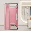 A pink changing room with a bench inside, set up in a retail store environment next to a clothing display. Voir les images du produit