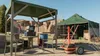 An outdoor setup with a tent, a covered area with a table and chairs, and some equipment. Náhľad obrázku produktu