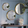 Three round mirrors with gold frames are mounted on a light blue wall above a wooden shelf. The shelf holds a stack of books, a decorative hourglass lamp, and a sculpture of a hand. Produktbild-Vorschau