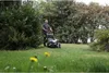 A man is mowing a lawn with a self-propelled lawnmower in a garden setting. Produktbild-Vorschau