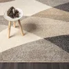 A close-up view of a geometric patterned rug with pine cones on a small stool. Produktbild-Vorschau