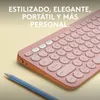 A close-up shot of a pink Logitech keyboard with a blue pencil in the foreground, set against a light yellow background. Produktbild-Vorschau