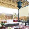A balcony or patio area furnished with a sofa, rug, table, and chair, under a striped awning. Náhled obrázku produktu
