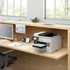 A modern office desk with a Canon MAXIFY GX 7050 Multifunktionsdrucker, computer monitor, and other office supplies. Produktbild-Vorschau