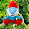 A plush toy of Papa Smurf sitting on mossy ground with green foliage in the background. Produktbild-Vorschau