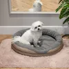 A small white dog sits in a round pet bed on a pink fluffy rug, with a mirror reflection of the dog in the background. Produktbild-Vorschau