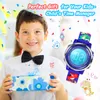 A young boy in a party hat and bow tie smiles while holding a gift. He is wearing a blue digital watch with dinosaur graphics. The background is festive with confetti and balloons. Produktbild-Vorschau