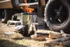 A rocket stove is burning in a campsite next to a vehicle. Produktbild-Vorschau