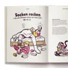 An open book showing an illustration of a mother and child playing with socks on a bed, with text describing a game. Produktbild-Vorschau