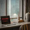 A desk with a laptop, lamp, books, and a vase, with a city view through the window. Produktbild-Vorschau