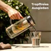 A hand is pouring water from a glass pitcher with fruit into a glass. Produktbild-Vorschau