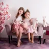 Two young girls sitting on a pink couch with stuffed toys. Produktbild-Vorschau