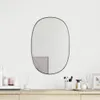 A black framed oval mirror hangs on a white wall above a wooden dresser with various toiletries and decorative items. Produktbild-Vorschau
