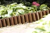 A garden border made of brown plastic, separating a paved area from a garden bed with hosta plants and a pink flower. Produktbild-Vorschau