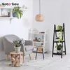 A cozy living room corner with a gray armchair, a wooden plant stand, and shelves filled with plants and decor. Produktbild-Vorschau