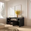 A modern living room with a black sideboard featuring an electric fireplace, two large abstract artworks on the wall, and a large window with a view of bare tree branches. Produktbild-Vorschau