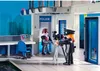 A Playmobil police station interior scene with two figures, one operating a camera and the other standing near a 'POLICE' sign. Produktbild-Vorschau