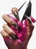 A hand with long, metallic silver nails holds a pink, faceted perfume bottle. Produktbild-Vorschau
