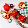 A collection of red bell peppers, red onions, garlic, and a jar of pickled peppers on a wooden cutting board. Produktbild-Vorschau