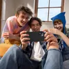 Three young people are looking at a smartphone held by one of them, laughing. Produktbild-Vorschau