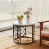 A round side table with decorative metal legs sits on a jute rug next to a leather armchair, with a window and sheer curtains in the background. Produktbild-Vorschau