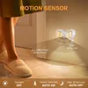 A person wearing slippers walks past a butterfly-shaped motion-activated night light mounted on a wall. Produktbild-Vorschau