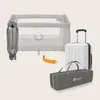 A baby travel cot is shown folded into a carrying bag next to a suitcase, illustrating its portability. Produktbild-Vorschau