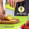 A person is using a wavy vegetable cutter to slice a potato on a wooden cutting board. There are tomatoes and a bottle of oil in the background. Produktbild-Vorschau