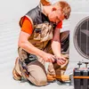 A technician is kneeling and working on an outdoor air conditioning unit. Produktbild-Vorschau