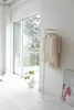 A minimalist interior scene with a clothing rack holding several garments, a potted plant, and a large window overlooking trees. Anteprima dell’immagine prodotto