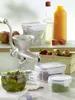 A collection of food preservation items including a manual juicer, jars of pickles and peas, a basket of strawberries, and bottles of juice and oil. Produktbild-Vorschau