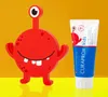 A red cartoon monster toy and a tube of toothpaste are displayed against a yellow and orange background. Anteprima dell’immagine prodotto