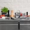 A professional kitchen setting with a tomato slicer, vegetables, and seasoning shakers. Voir les images du produit
