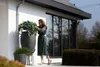 A woman tending to plants in large decorative pots outside a modern house. Anteprima dell’immagine prodotto
