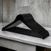 A stack of black wooden hangers with silver metal hooks is displayed on a marbled surface, with a textured gray wall in the background. Produktbild-Vorschau