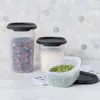 Three clear plastic food storage containers with black lids are arranged on a marble countertop in front of a hexagonal tiled backsplash. Anteprima dell’immagine prodotto