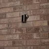 A silver outdoor wall lamp is mounted on a brick wall. Produktbild-Vorschau