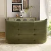 A green sofa is shown in a living room setting with a cabinet and artwork in the background. Produktbild-Vorschau