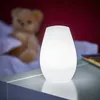 A white LED lamp is placed on a nightstand next to a teddy bear in a dimly lit room. Produktbild-Vorschau