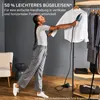 A woman is using a handheld garment steamer on a white shirt hanging on a rack, with other clothes on the rack and shelves. Anteprima dell’immagine prodotto
