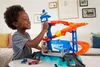A young boy is playing with a Hot Wheels shark-themed car track set indoors. Produktbild-Vorschau