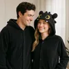 A couple wearing matching black onesies with dragon-themed hoods, smiling at each other. Anteprima dell’immagine prodotto