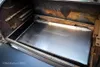 The interior of a grill with a stainless steel drip pan. Produktbild-Vorschau