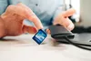 A person is holding an SD card over a desk with a card reader and laptop in the background. Produktbild-Vorschau