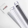 A close-up shot of two clear plastic shower door seals with black magnetic strips, placed diagonally on a white background. A white card with the brand logo is visible in the background. Produktbild-Vorschau